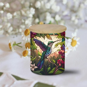 May include: A cylindrical glass candle jar with a wooden lid. The jar features a stained glass design of a hummingbird with green, blue, and purple feathers, perched on a branch with red berries. The background is a vibrant green with a stained glass effect.
