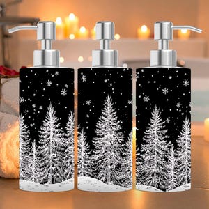May include: Three black and white soap dispensers with silver pump tops. The dispensers feature a winter forest scene with white pine trees and snowflakes against a black background. The dispensers are cylindrical and sit on a light-colored surface.