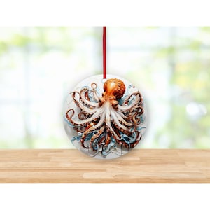 May include: A round, white ornament with a red string for hanging. The ornament features a detailed painting of an orange octopus with white tentacles against a blue and white background.