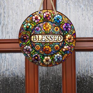 May include: Round, stained-glass style wall hanging with a floral design in shades of blue, purple, orange, and green. The word "BLESSED" is displayed in the center. A natural rope is attached for hanging.