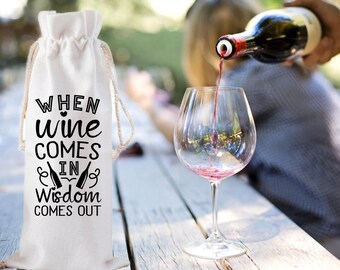 May include: A white wine bottle bag with the text "WHEN WINE COMES IN WISDOM COMES OUT" in black. A person is pouring red wine into a clear wine glass. The bag has a drawstring closure.