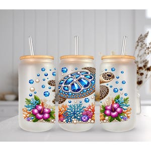 May include: Three frosted glass tumblers with bamboo lids and metal straws. Each features a sea turtle design with blue gemstone-like accents, colorful coral, and pink hibiscus flowers. The artwork is repeated across the three glass cups.