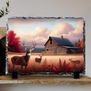 May include: A rectangular slate art piece featuring a pastoral scene with deer and a barn. The artwork depicts a brown buck with large antlers, two smaller deer, and a weathered wooden barn under a cloudy sky. The color palette includes browns, reds, and yellows.