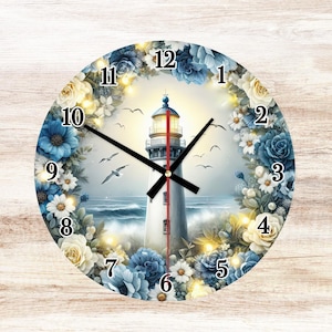 May include: Round wall clock featuring a lighthouse scene with blue and white flowers. The clock face displays black hands and numerals. The lighthouse is white with a red top, set against a seascape with flying birds. The clock is surrounded by a floral wreath.