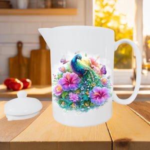 May include: White ceramic pitcher with a peacock and floral design. The peacock has blue, green, and teal feathers, surrounded by pink and purple flowers and butterflies. The pitcher has a handle and a separate lid.