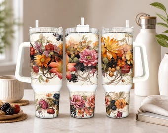 Könnte beinhalten: Drei Edelstahlbecher mit Griffen und Strohhalmen, jeweils mit einem umlaufenden Blumenmuster aus orangefarbenen, rosafarbenen und roten Blüten, grünen Blättern, dunklen Beeren und einem kleinen Schmetterling auf cremefarbenem Grund.