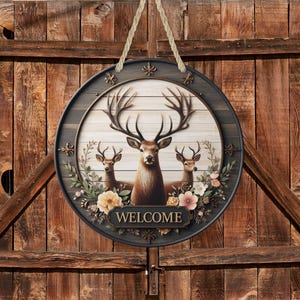 Op de afbeelding: Ronde houten welkomstbord met een illustratie van een hertenfamilie. Het bord heeft een donker frame met bloemaccenten en het woord "WELCOME" onderaan. De achtergrond is een licht houtnerfpatroon.