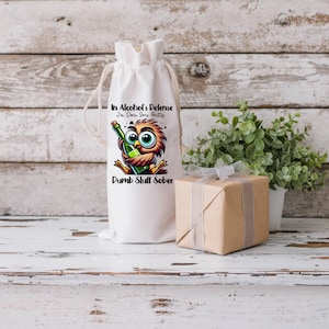 May include: White fabric wine bottle bag with a cartoon owl holding a bottle of wine. The bag has the text "In Alcohol's Defense I'm Sure I'm Pretty Dumb Stuff Sober".
