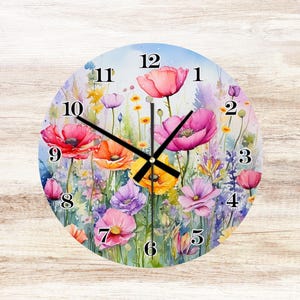 May include: Round wall clock featuring a watercolor floral design with poppies and wildflowers in shades of pink, orange, yellow, and purple. The clock face has black hands and black numerals against a light blue background.