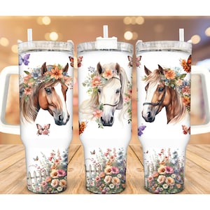 May include: White insulated tumbler featuring three horse head designs with floral crowns and butterflies. The bottom of the tumbler has a floral garden design with a white picket fence. The tumbler has a white handle and a clear lid with a straw.