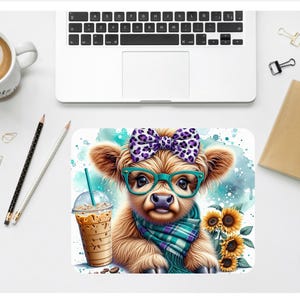 May include: A rectangular mousepad featuring a cartoon Highland cow with a purple bow, teal glasses, and a plaid scarf. The cow is holding an iced coffee and is surrounded by sunflowers. The background has a watercolor effect with teal and blue hues.