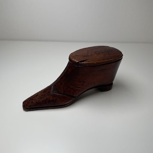 May include: A wooden shoe-shaped box with a hinged lid. The box is made of dark brown wood and has a simple, elegant design.