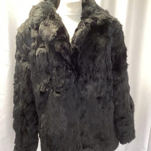 May include: A black fur coat with a wide collar, displayed on a white mannequin. The fur has a soft, plush appearance with a slightly textured look. The coat's design is classic and timeless.