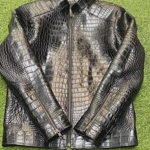 Könnte beinhalten: Eine schwarze Jacke aus Krokodilleder mit Reißverschluss. Die Jacke hat einen Stehkragen und lange Ärmel.