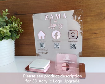 May include: A clear acrylic display stand with rose gold detailing. The stand displays the text "ZAMA & Legacy" and social media icons. It includes a card holder and a payment terminal. The text "Shop Online! afterpay" is also visible.