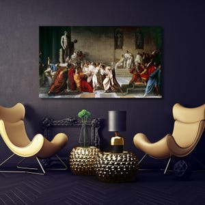 May include: A framed canvas print of a classical painting showing a dramatic scene with figures in robes. The artwork is displayed above two gold accent chairs and two gold side tables with a black lamp.