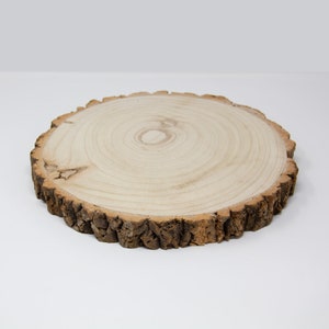 May include: A round wooden slice with a natural bark edge. The wood is light brown and has a natural grain pattern.