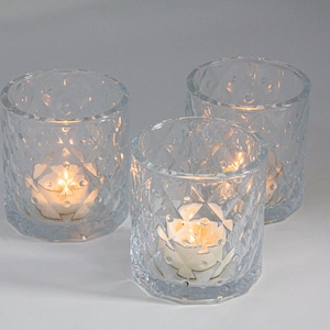 May include: Three clear glass candle holders with a diamond pattern. Each holder has a white tea light candle inside.