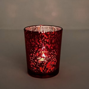 May include: A red glass candle holder with a speckled finish. The holder is lit with a candle inside.