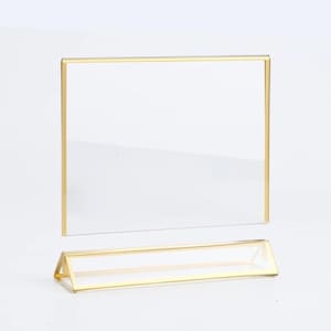 May include: A gold-coloured acrylic sign holder with a clear acrylic sign. The sign holder has a triangular base.