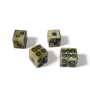 May include: Four antique dice with black dot markings on a cream-coloured surface. The dice are arranged at different angles, showcasing the various number combinations. The dice appear to be made of bone or a similar material.