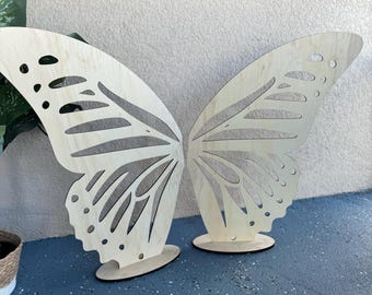 May include: Two large wooden butterfly wings with intricate cutouts, standing on small wooden bases. The wings are light brown and have a natural wood finish.