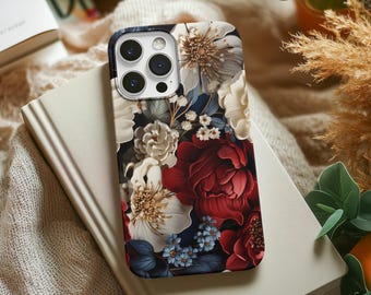 Può includere: Una custodia per telefono floreale con sfondo scuro e fiori rossi, bianchi e blu. La custodia è appoggiata su un libro chiuso con copertina beige. La custodia del telefono ha una finitura lucida.