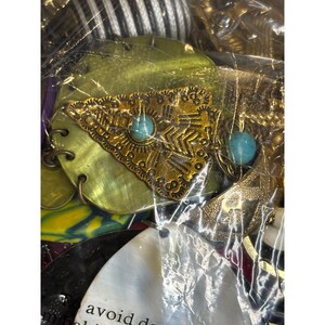 May include: A close-up of a collection of jewelry featuring a large gold pendant with turquoise stones. The pendant is in the shape of a triangle with intricate designs. The jewelry is displayed on a white background.