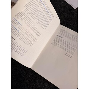 Op de afbeelding: Een open boek met tekst op de pagina's. De linkerpagina heeft een lijst met opsommingstekens en de rechterpagina heeft de titel "The Authors" met tekst eronder. Het boek ligt op een donkere ondergrond.