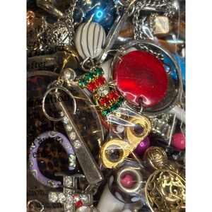 May include: A close-up of a variety of colorful beads, charms, and jewelry pieces in a clear plastic bag. The items include a red round bead, a gold charm with a pair of glasses, a silver charm with rhinestones, and a green and red charm with a Christmas stocking design.