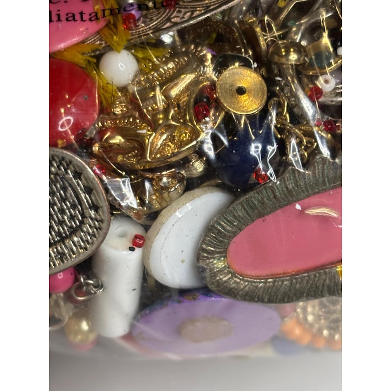 May include: A close-up of a variety of colorful buttons and beads in a clear plastic bag. The buttons are made of metal, plastic, and ceramic. The beads are made of glass, plastic, and wood. The colors include red, blue, green, yellow, and white.