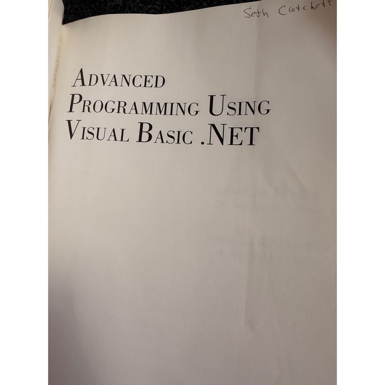 Op de afbeelding: Open boek met de titel "ADVANCED PROGRAMMING USING VISUAL BASIC .NET" in grote, zwarte letters. De naam van de auteur, Seth Crotchett, is met de hand geschreven rechtsboven. De pagina's zijn gebroken wit.