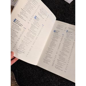 Op de afbeelding: Open boek met pagina's met tekst. De linkerpagina toont de titel "Windows Database Using Related Tables". De rechterpagina heeft de titel "Using Web Forms ASP.NET". De pagina's zijn wit met zwarte tekst.