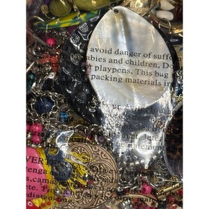 May include: A close-up of a variety of colorful jewelry and trinkets, including a large white shell with the text "avoid danger of suffocation babies and children, Do not use in cribs, beds, carriages or playpens, This bag is not a toy. Keep away from packing materials inside."