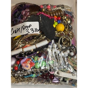 May include: A plastic bag filled with a variety of colorful beads, chains, and other craft supplies. The bag is labeled "Craft/Scrap 3.3lb".