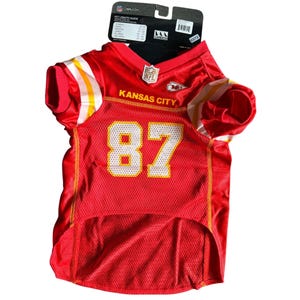 May include: Red pet jersey with white and yellow accents, featuring the number 87 in yellow. The jersey has the text "Kansas City" and the NFL logo. A tag with pet length guide is attached.