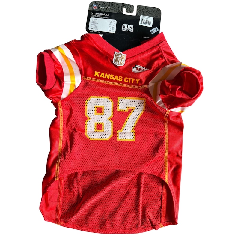May include: Red pet jersey with white and yellow accents, featuring the number 87 in yellow. The jersey has the text "Kansas City" and the NFL logo. A tag with pet length guide is attached.