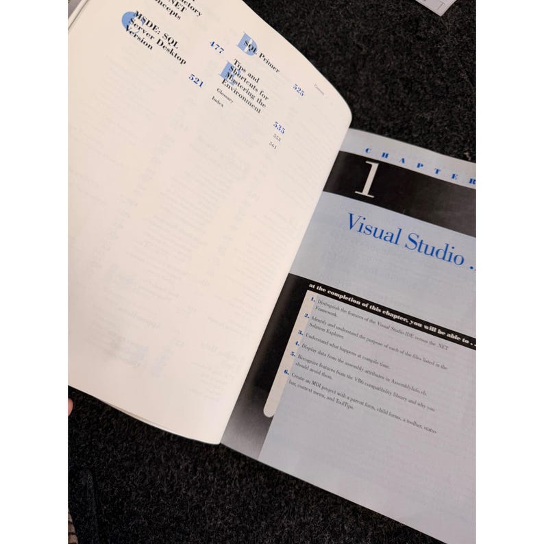 Op de afbeelding: Open boek met de titel "Visual Studio" op de rechterpagina. De linkerpagina heeft een lijst met onderwerpen. Het boek ligt open op een donkere ondergrond.