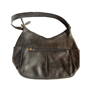 Puede incluir: Bolso de hombro de cuero gris oscuro con una sola correa. El bolso tiene forma curva con un bolsillo con cremallera en la parte trasera y un bolsillo pequeño en la parte delantera. La cremallera y los herrajes son dorados.