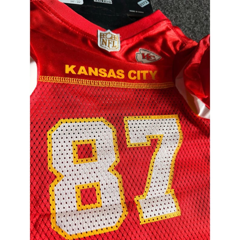 May include: A red mesh jersey with the words "KANSAS CITY" in yellow lettering. The number "87" is prominently displayed in white with yellow trim. An NFL logo is visible.