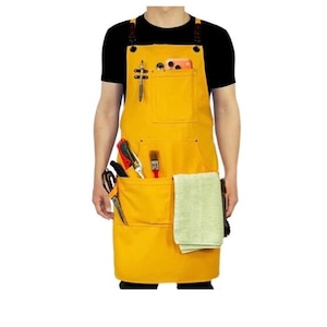 May include: A mustard yellow apron with multiple pockets and leather straps. The apron has a pocket for a phone, pens, and tools. A light green towel hangs on the side. The apron is worn over a black shirt.