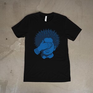 Peut inclure: T-shirt noir avec un motif bleu d'une personne dont les yeux sont couverts par une main. La personne a des cheveux bouclés bleus et porte une chemise à col. Le motif est de couleur bleu uni.