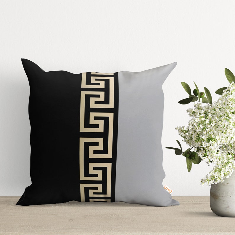 Black and gray throw pillow with a gold Greek key pattern down the center.