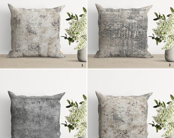 May include: Four different decorative throw pillows with a distressed, abstract pattern in shades of gray, beige, and white. The pillows are arranged in a grid pattern on a wooden surface.