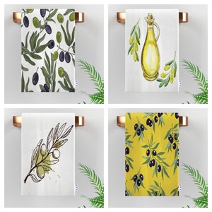 Four kitchen towels with different olive branch designs. One towel features a green olive branch with black olives, another has a green olive branch with a yellow olive oil bottle, another has a black and white olive branch, and the last one has a yellow olive branch with black olives.