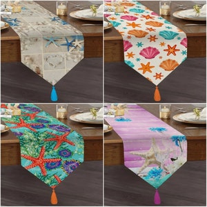 May include: Four table runners with different beach-themed designs. The first runner features a white background with seashells and starfish. The second runner has a white background with orange and pink seashells and starfish. The third runner has a turquoise background with orange starfish and coral. The fourth runner has a purple background with a whitewashed wood design and a starfish.