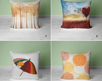 May include: Four different throw pillow designs featuring autumnal themes. The first pillow has a pattern of orange and yellow trees. The second pillow has a red heart-shaped tree with red leaves on the ground. The third pillow has a colorful umbrella with a maple leaf on top. The fourth pillow has a pattern of orange and yellow flowers.