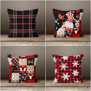May include: Four decorative throw pillows with holiday themes. Designs include a black and red plaid, a snowman with a red scarf and hat, a patchwork design with axes and deer, and a red plaid with white snowflakes.