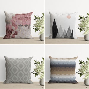 May include: Four different decorative cushion covers with geometric patterns. The first cushion cover has a pink and gold geometric pattern. The second cushion cover has a black and white mountain range pattern. The third cushion cover has a grey and white geometric pattern. The fourth cushion cover has a blue, brown, and white geometric pattern.