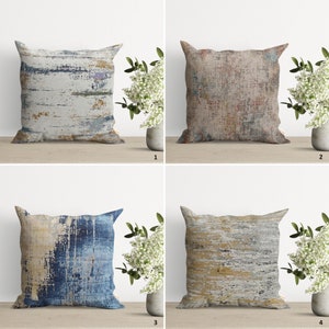 Pu&ograve; includere: Quattro cuscini decorativi con motivi astratti in tonalit&agrave; di blu, marrone, giallo e grigio. I cuscini sono disposti in una griglia su una superficie in legno.